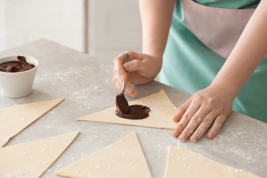 Woman preparing tasty croissants with chocolate paste on table, closeup