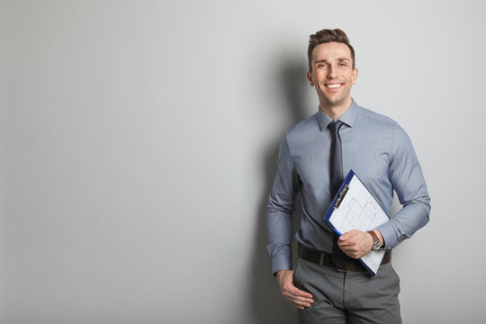 Male Real Estate Agent With Clipboard On Grey Background