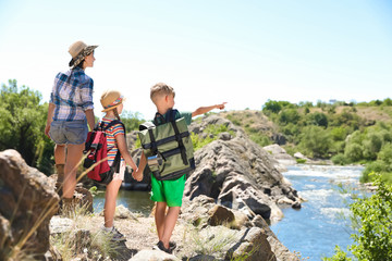 Young woman with children on rock near river. Summer camp