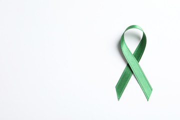 Green ribbon on white background, top view. Cancer awareness