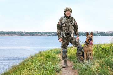 Man in military uniform with German shepherd dog near river