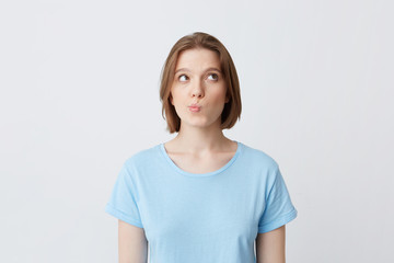 Fototapeta premium Portrait of pensive pretty young woman in blue t shirt thinking and feels puzzled isolated over white background Looks to the side nd frowning her face