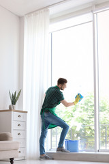 Male worker washing window glass at home