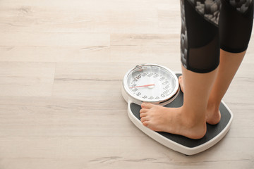 Woman measuring her weight using scales on wooden floor. Healthy diet