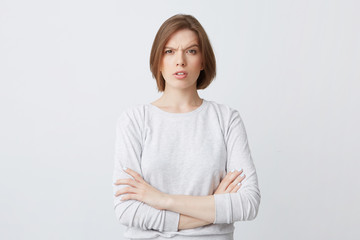 Portrait of serious confused young woman in longsleeve standing with arms crossed and looking...