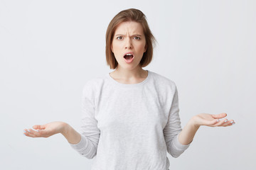 Angry puzzled young woman with opened mouth in longsleeve looking shocked and holding copyspace on...