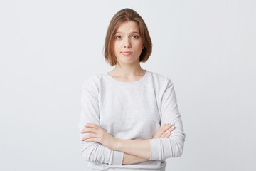 Unhappy dissatisfied young woman in longsleeve standing with hands folded and feels disappointed isolated over white background - obrazy, fototapety, plakaty