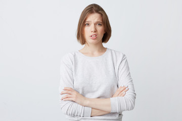 Portrait of upset disappointed young woman in longsleeve standing with arms crossed and looks dissatisfied isolated over white background
