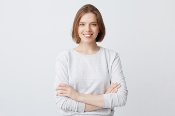 Smiling beautiful young woman in longsleeve standing with arms crossed and feeling confident isolated over white background Looks successful - Powered by Adobe