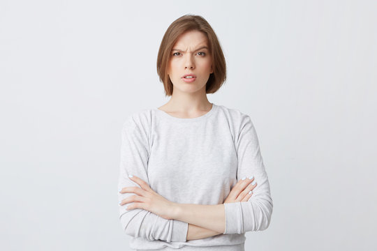 Portrait of serious confused young woman in longsleeve standing with arms crossed and looking confused isolated over white background Feels puzzled