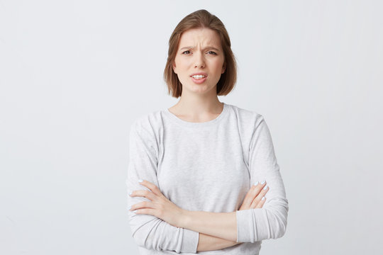 Closeup of angry annoyed young woman in longsleeve standing with arms crossed and feels irritated isolated over white backgound Looks directly in camera