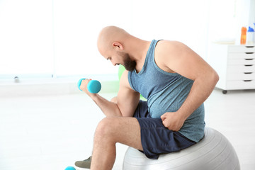 Fototapeta na wymiar Overweight man doing exercise with dumbbell in gym
