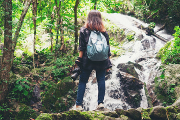 Naklejka na ściany i meble Traveler young woman photographing with camera near the waterfall outdoor