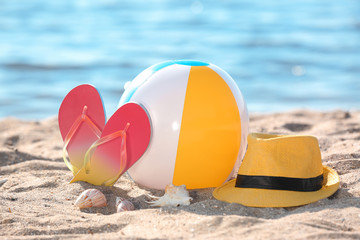 Inflatable ball, hat and flip flops on sand near sea. Beach object