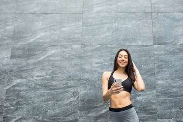 Young woman relaxing after jogging. She using her smart phone Typing message leaning against outdoors wall.