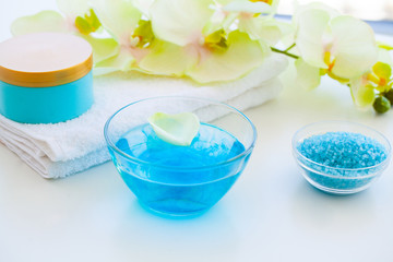 Obraz na płótnie Canvas Organic Blue Sea Salt. Spa Composition With Cream, Salt, Towel and Flowers On a White Background. Wellness Products and Cosmetics.