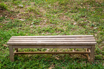 Long wood bench on the grass field close up.