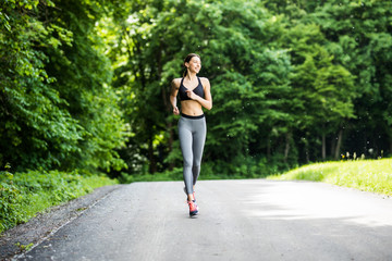 Fototapeta na wymiar Young lady running. Woman runner running through the spring park road. Workout in a Park. Beautiful fit Girl. Fitness model outdoors. Weight Loss