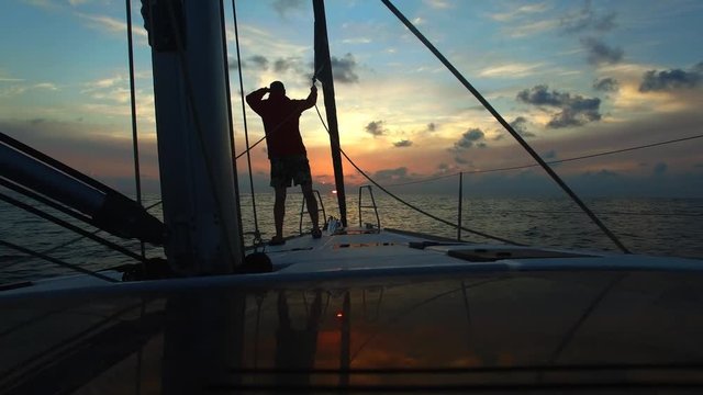Young man sailor are looking forward on deck sailing yacht at sunset . Freedom on the small ship.