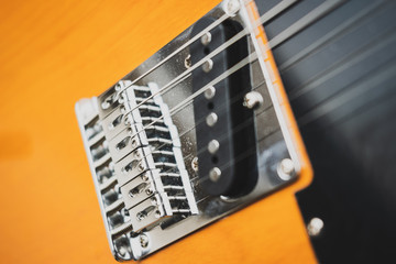 Details of an orange electric guitar with a vintage style, bridge and saddles.