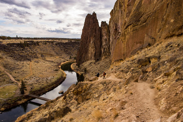 Two hikers descend a path to the river by some large rock formations, Oregon