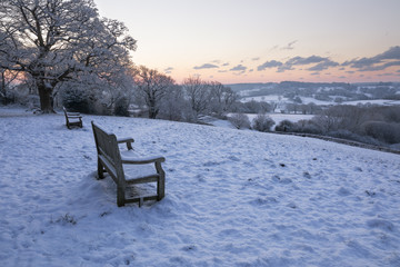 Bench overlooking snow covered High Weald landscape at sunrise, Burwash, East Sussex