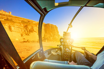 Helicopter cockpit interior flying on Azenhas do Mar beach at sunlight, the Atlantic Ocean in Portugal. Scenic flight above Popular Portuguese seaside skyline near Colares and Sintra municipality.