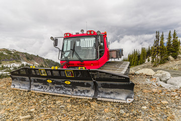 Fototapeta premium Red tractor, snow plough parked outside a mountain on the rocks