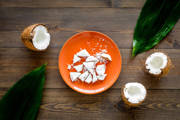 Coconut pulp on plate near cut coconut and palm leaves on dark wooden background top view copy space