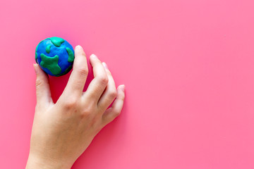 Earth. Hand hold plastiline symbol of planet Earth globe on pink background top view copy space