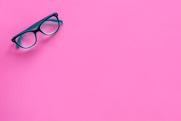 One glasses with transparent lenses on pink background top view copy space