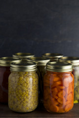 Various Types of Canned Vegetables on a Wooden Table in a Dark Environment
