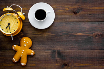 Time loss concept. Gingerbread man near alarm clock on dark wooden background top view space for text