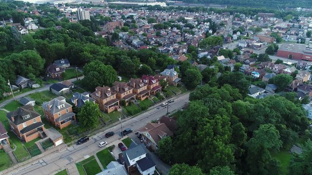 An aerial flyover establishing shot view of a small rust belt town and residential neighborhood in the early evening. Pittsburgh suburbs.  	