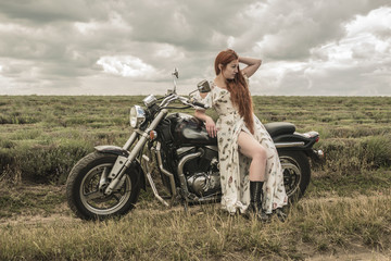 Fototapeta premium red-haired girl in a white dress and boots along with a motorcycle. lavender field