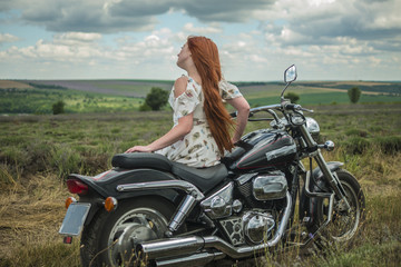 Obraz na płótnie Canvas red-haired girl in a white dress and boots along with a motorcycle. lavender field