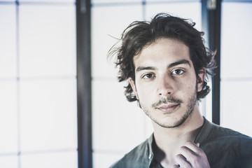 An handsome young man, 20Y, is posing in studio touching the collar of the skirt in a worried way . Green skirt. Retroilluminated booths in the background.