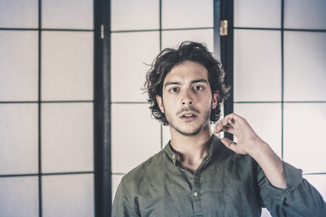 An handsome young man, 20Y, is posing in studio touching the head . Surprised expression. Green skirt. Retroilluminated booths in the background.