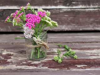 Glass with flowers achillea millefolium, commonly known as yarrow or common yarrow on rustic weathered wooden boards. Medicinal plant.Empty space for your text.