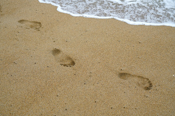 footprints on the beach sand with sea wave
