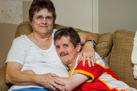 Man With Downs Syndrome Hugs His Older Sister On A Couch