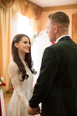 Portrait of the young beautiful couple who is standing indoor and looking at each other and holding hands in their wedding day