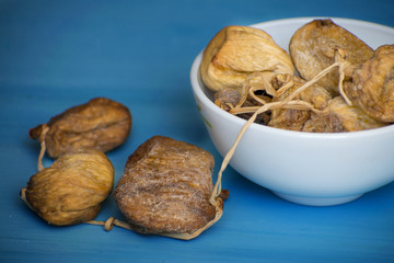Dried figs in a white bowl on a blue table. Dried fruit.