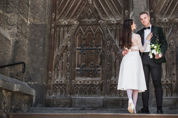 The romantic young stylish newlyweds standing in an embrace near the old build