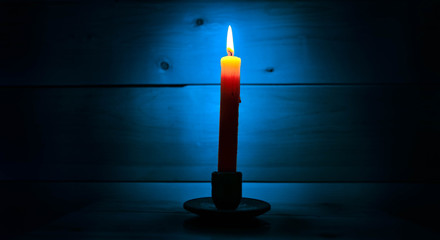 In the dark the candle burns orange and the light blue on the wall