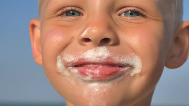 Little hungry boy eating ice cream on the beach of the sea. The baby's face is smeared with ice cream.