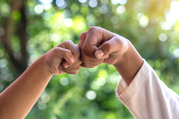 Hands fist bumps against green background blurred.
