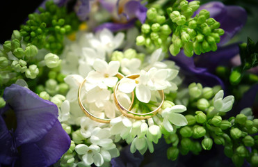 Wedding rings lie on flowers in a bouquet of white lilac and purple freesias