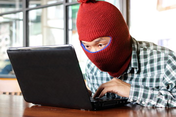 Masked hacker wearing a balaclava stealing importance data from laptop. Internet crime concept.