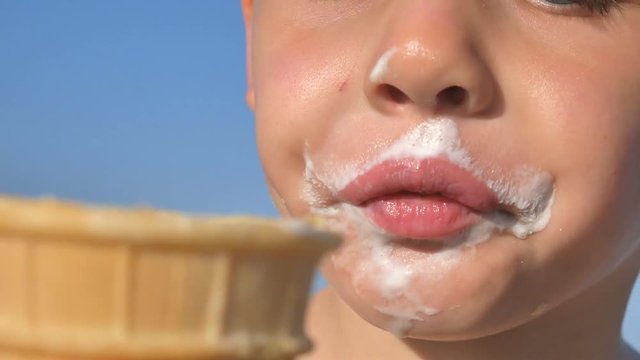 Little hungry boy eating ice cream on the beach of the sea. The baby's face is smeared with ice cream.